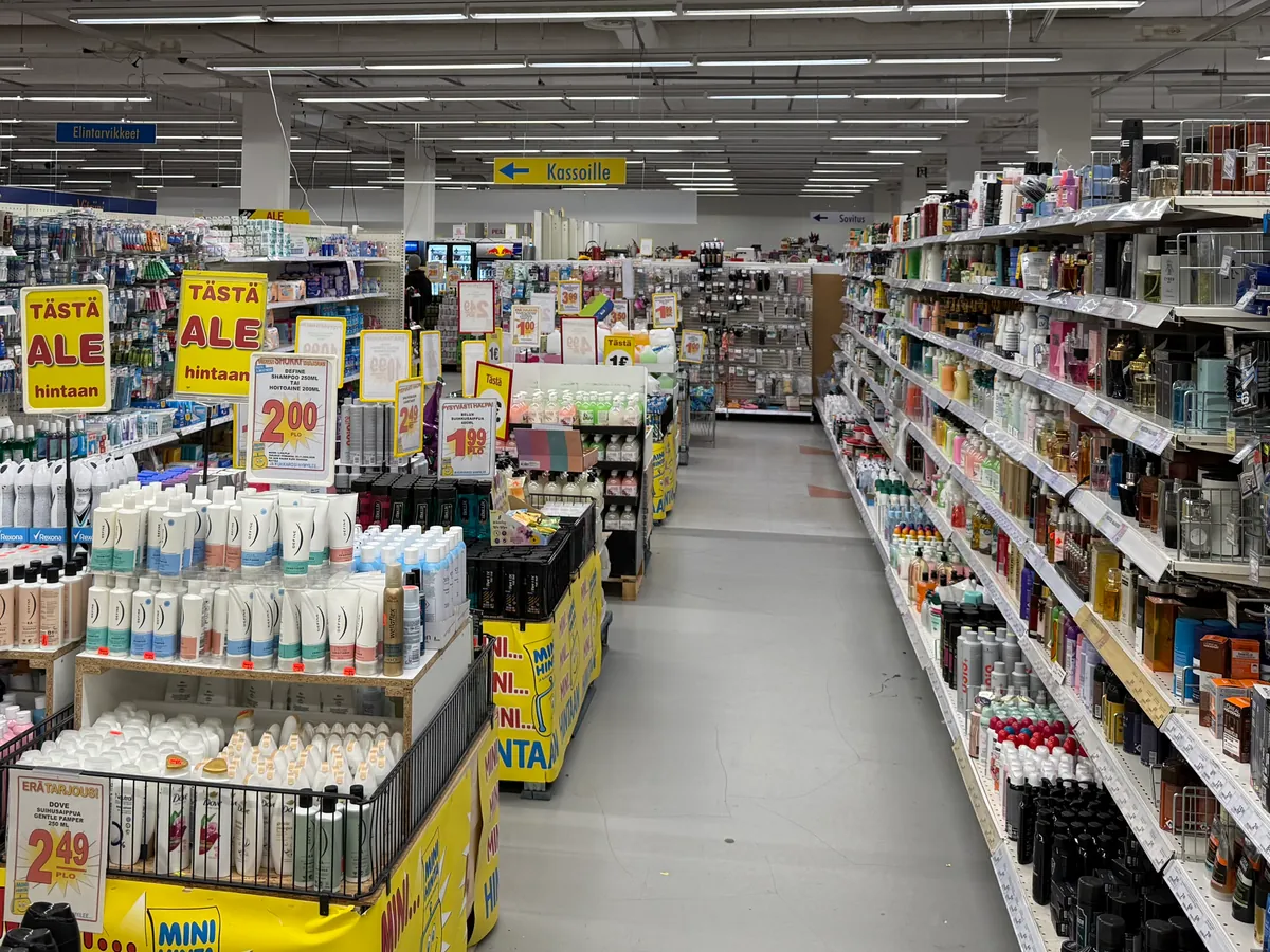 Hygieniatuotekäytävä: shampoot ja deodorantit hyllyissä, keskellä tarjouspöydät ja Tästä ALE -kyltit